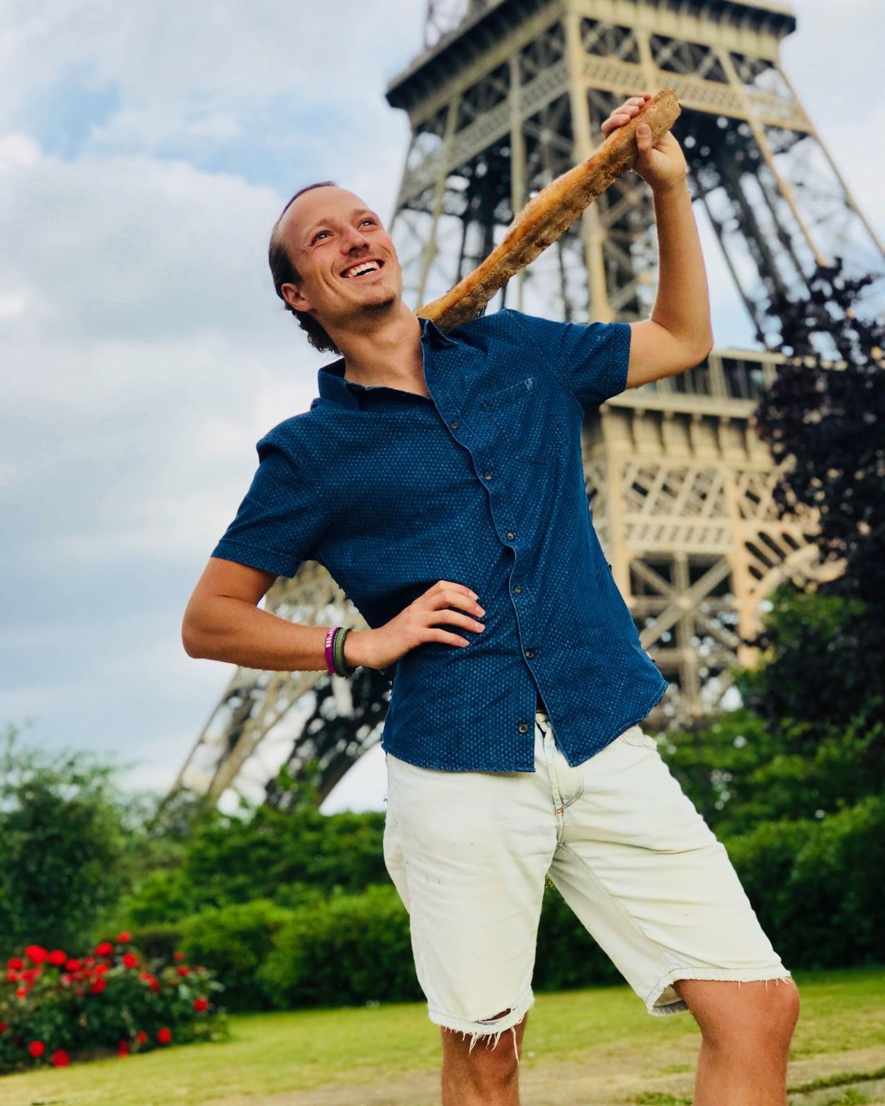 Gui grinning with a baguette on his shoulder below the Eiffel Tower
