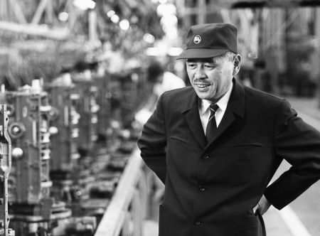 Taiichi Ohno in cap and coat beside a Toyota engine assembly line