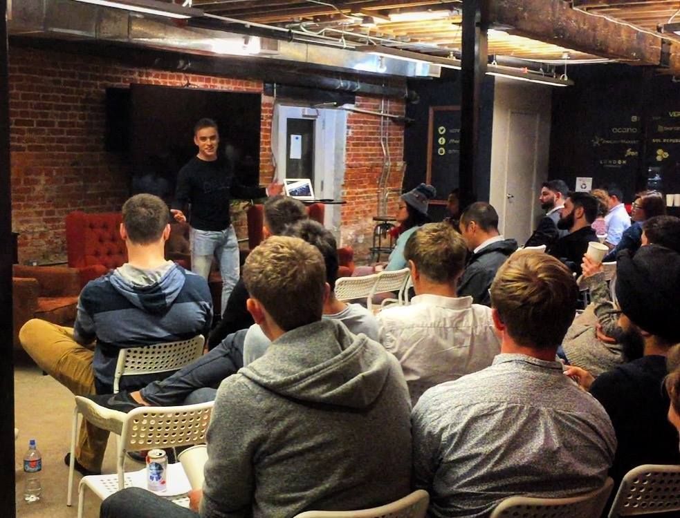Renat speaking to a seated crowd in a brick-walled event space