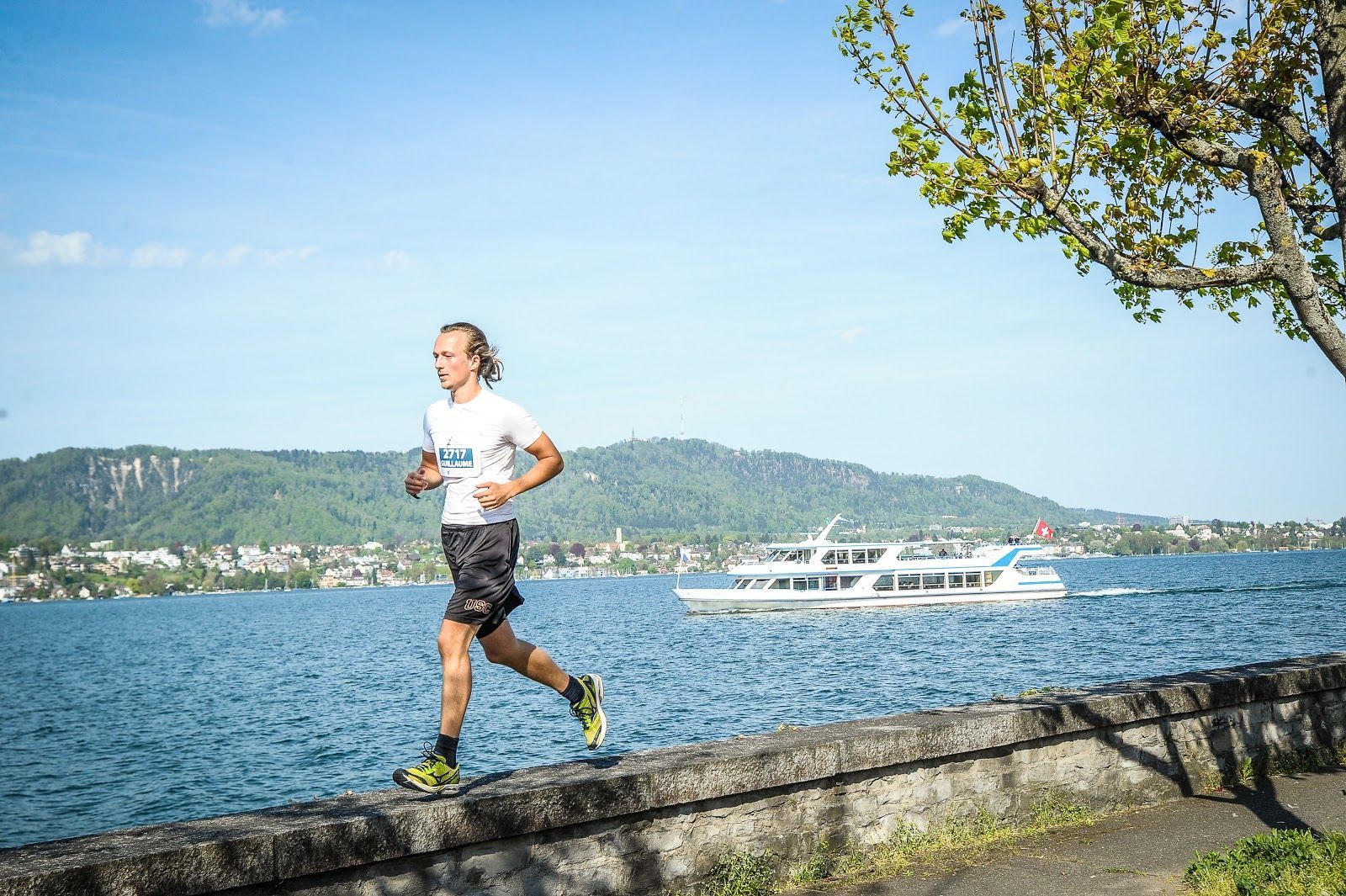 Gui running along a lakeside wall in Zurich, boat behind him