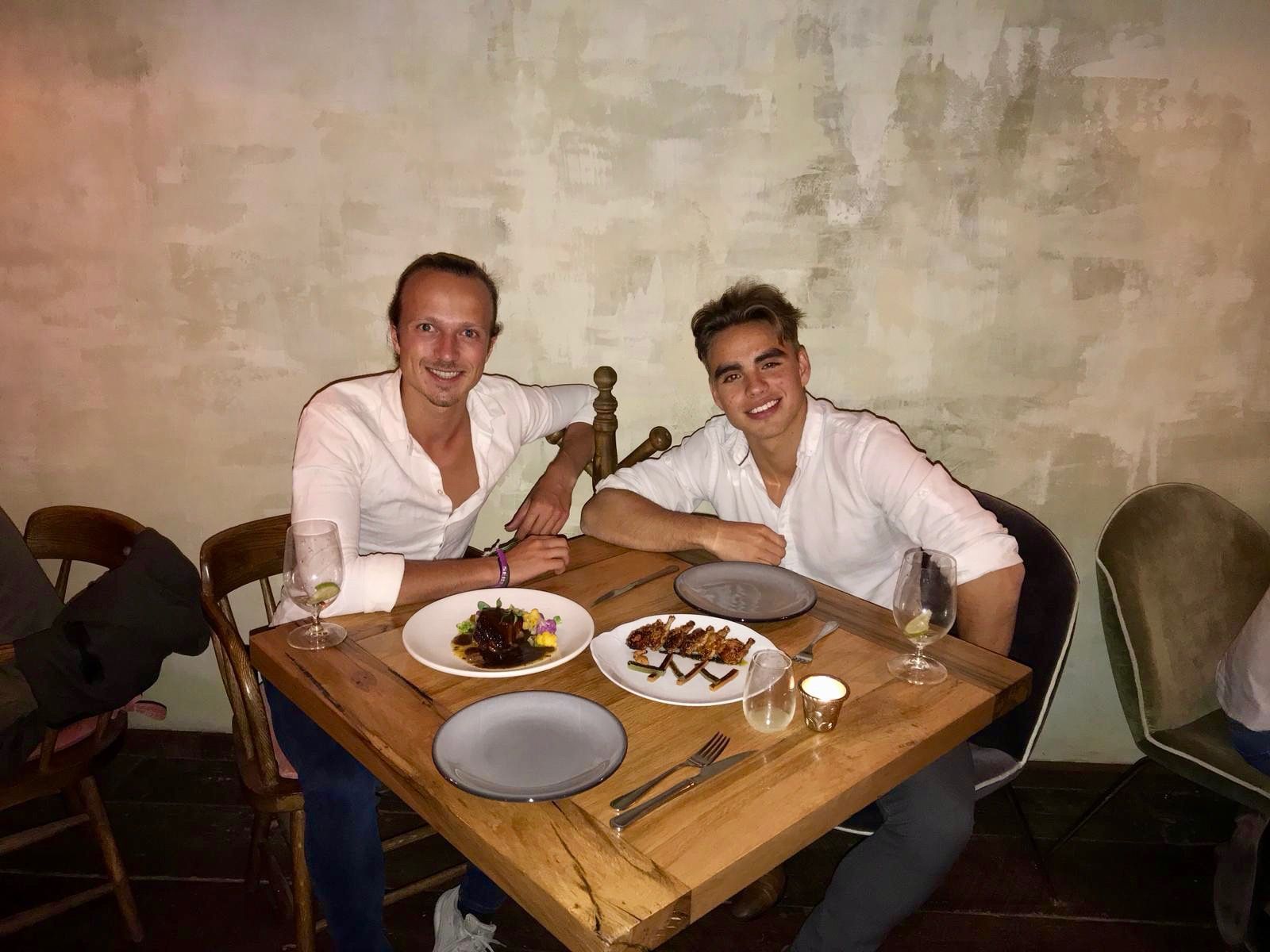 Gui and Renat in white shirts at a restaurant table, plates served